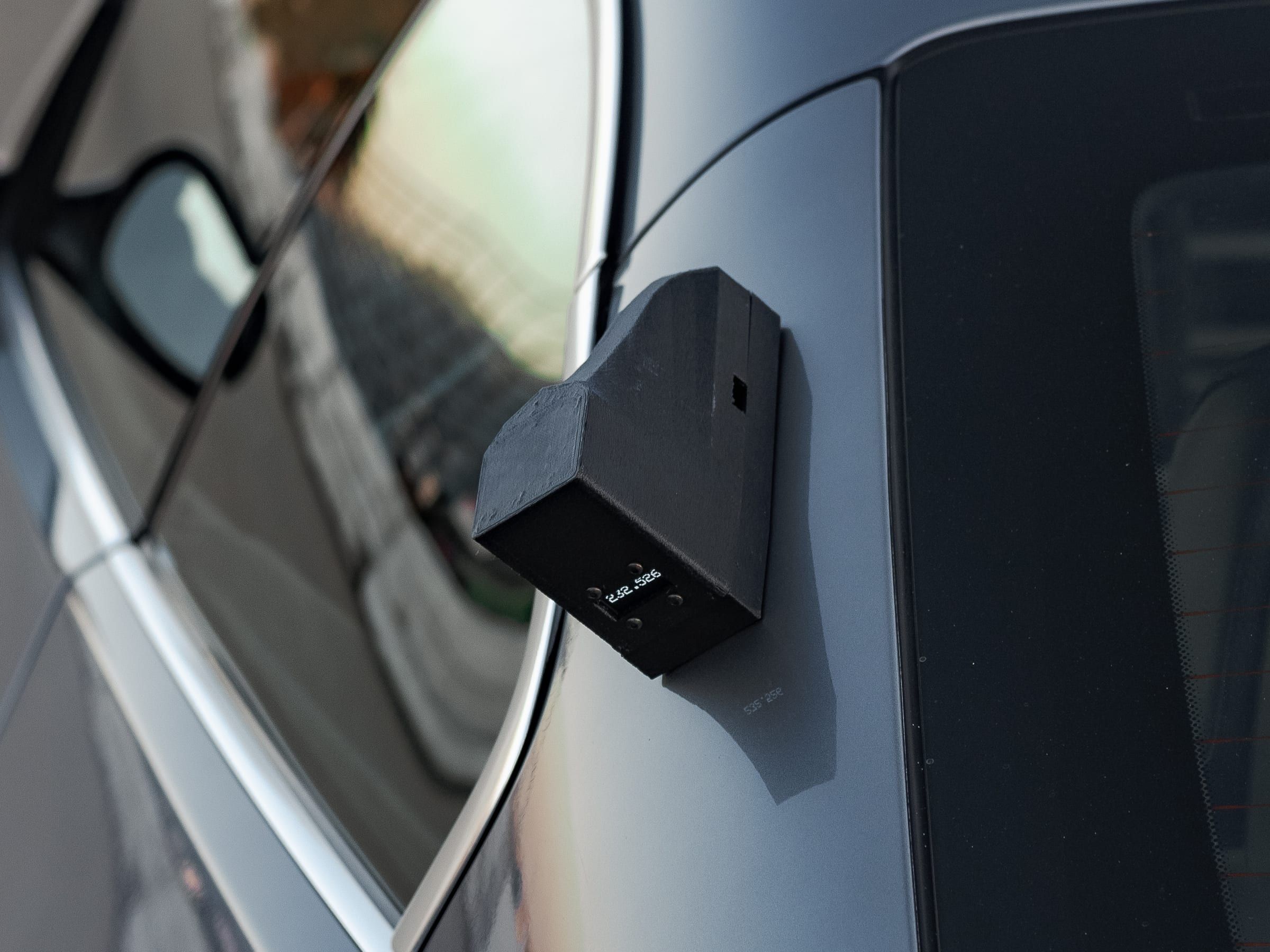 A timing unit with its display lit on the rear roof pillar of a grey coupe.
